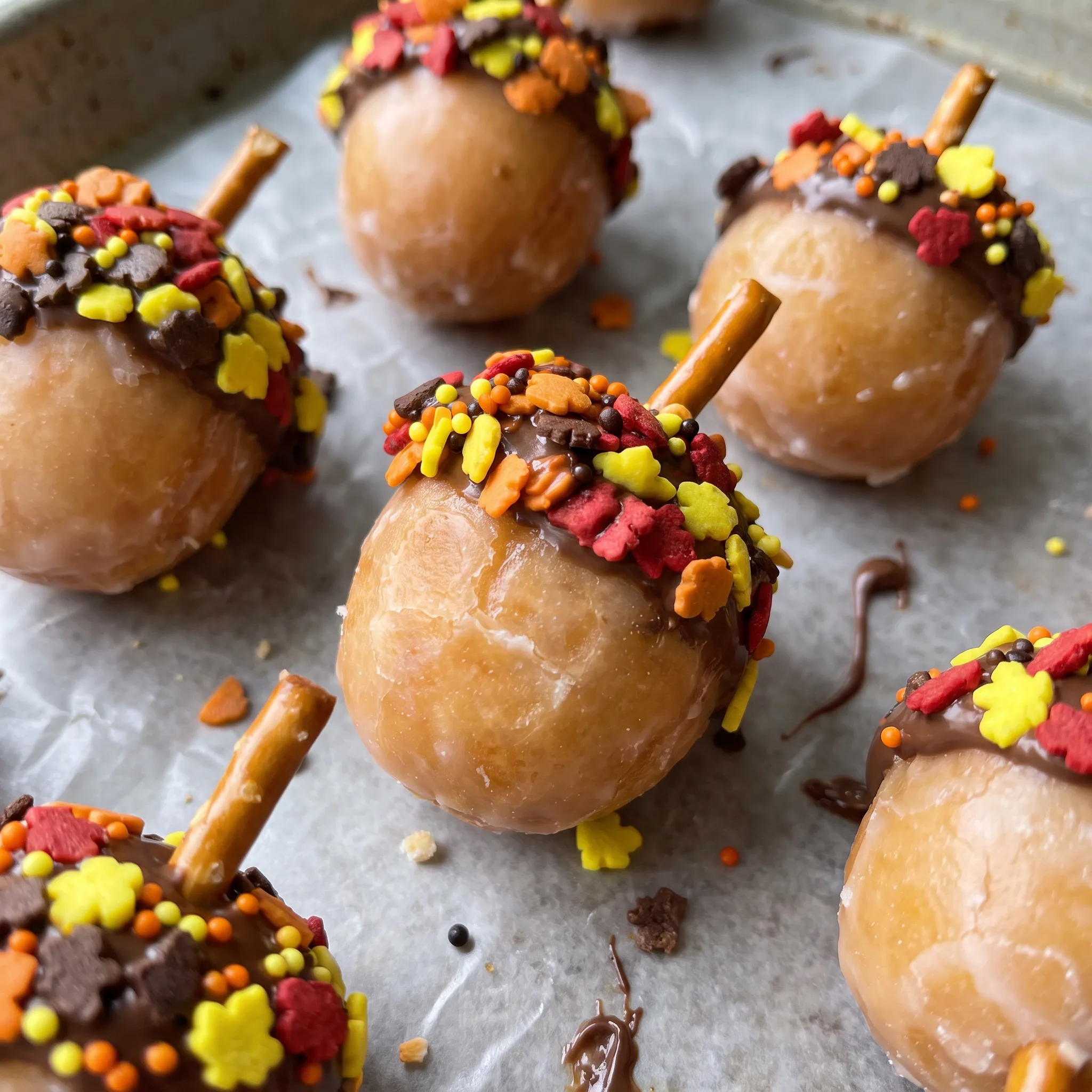 Glossy chocolate hazelnut spread over round donut holes, dotted with orange and brown sprinkles and a crisp pretzel stick.