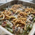 Green bean casserole with green beans, bacon, mushrooms, melted Monterey Jack cheese, and French fried onions on top.