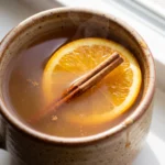 Spiced tea punch in amber orange with pineapple and lemon juice, cinnamon sticks and cloves floating on top.